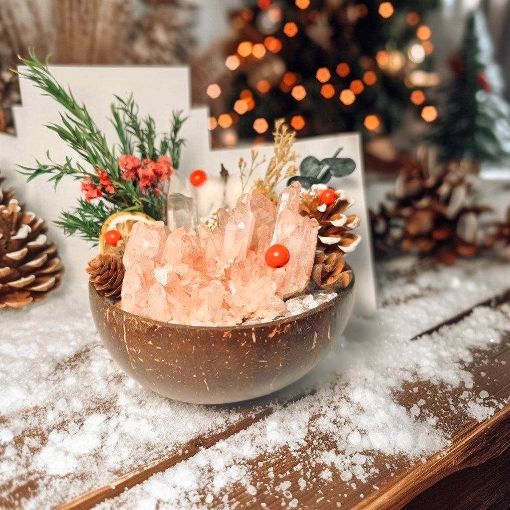 rose quartz crystal cluster mini garden in a coconut bowl on a snowy wooden table with pinecones and warm Christmas tree bokeh lights